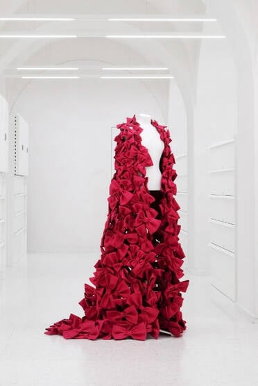 A mannequin bust draped with a coat made of red bows
