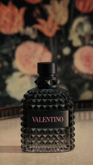 Bottle of BORN IN ROMA Uomo on table with floral wallpaper background