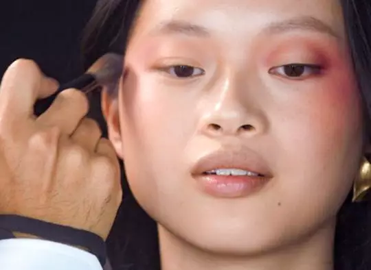 Makeup artists applying pink and orange eye makeup to a model