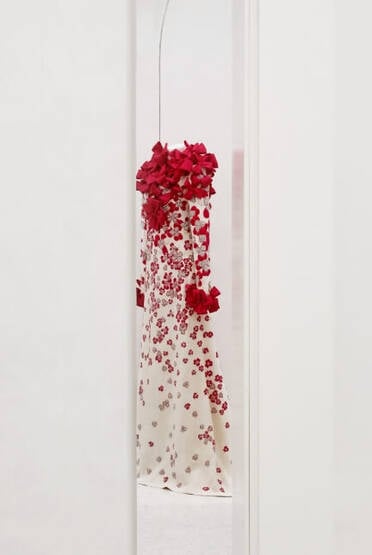 Mirror reflection of mannequin draped with white and red bows and flowers