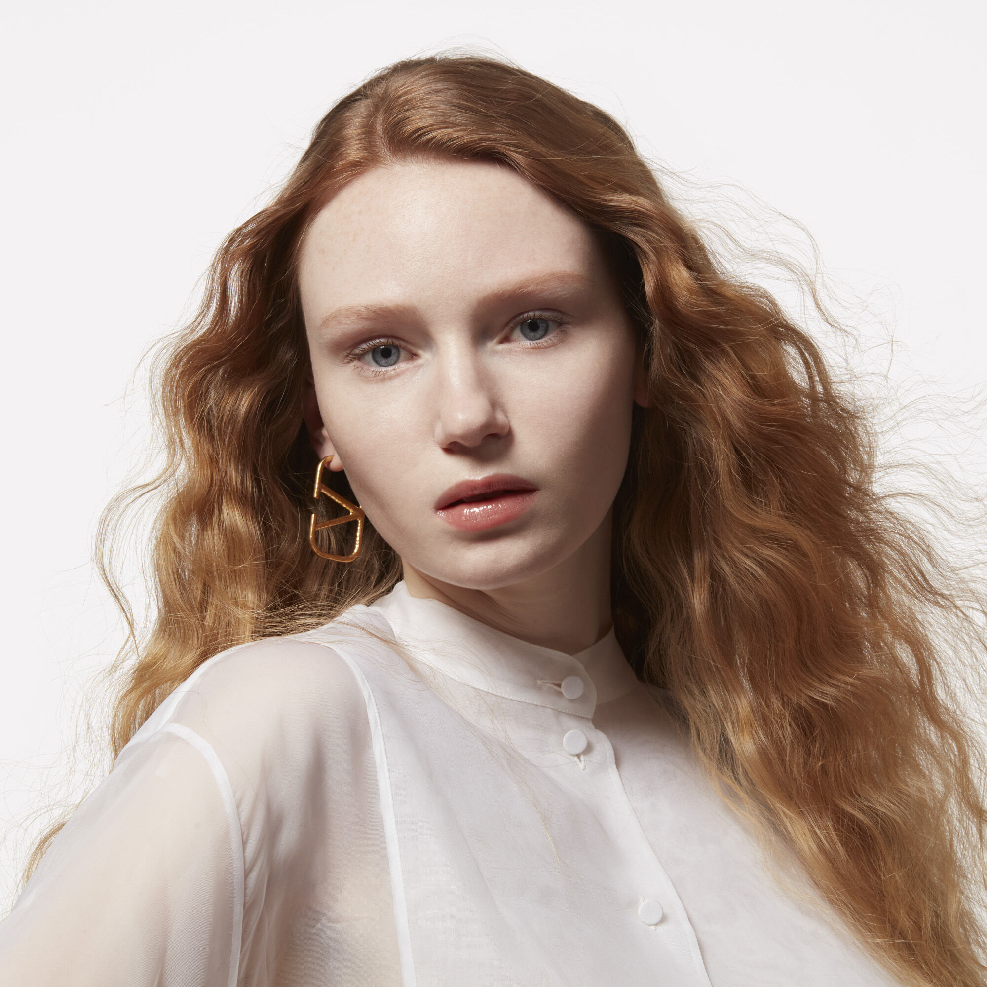 A model with wavy strawberry blonde hair wearing Valentino beauty logo earring