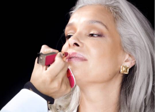 Makeup artist applying lipstick to model with long gray hair