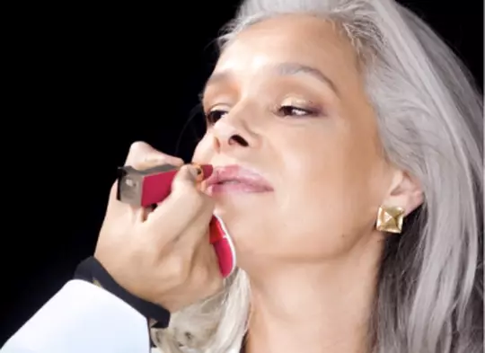 Makeup artist applying lipstick to model with long gray hair