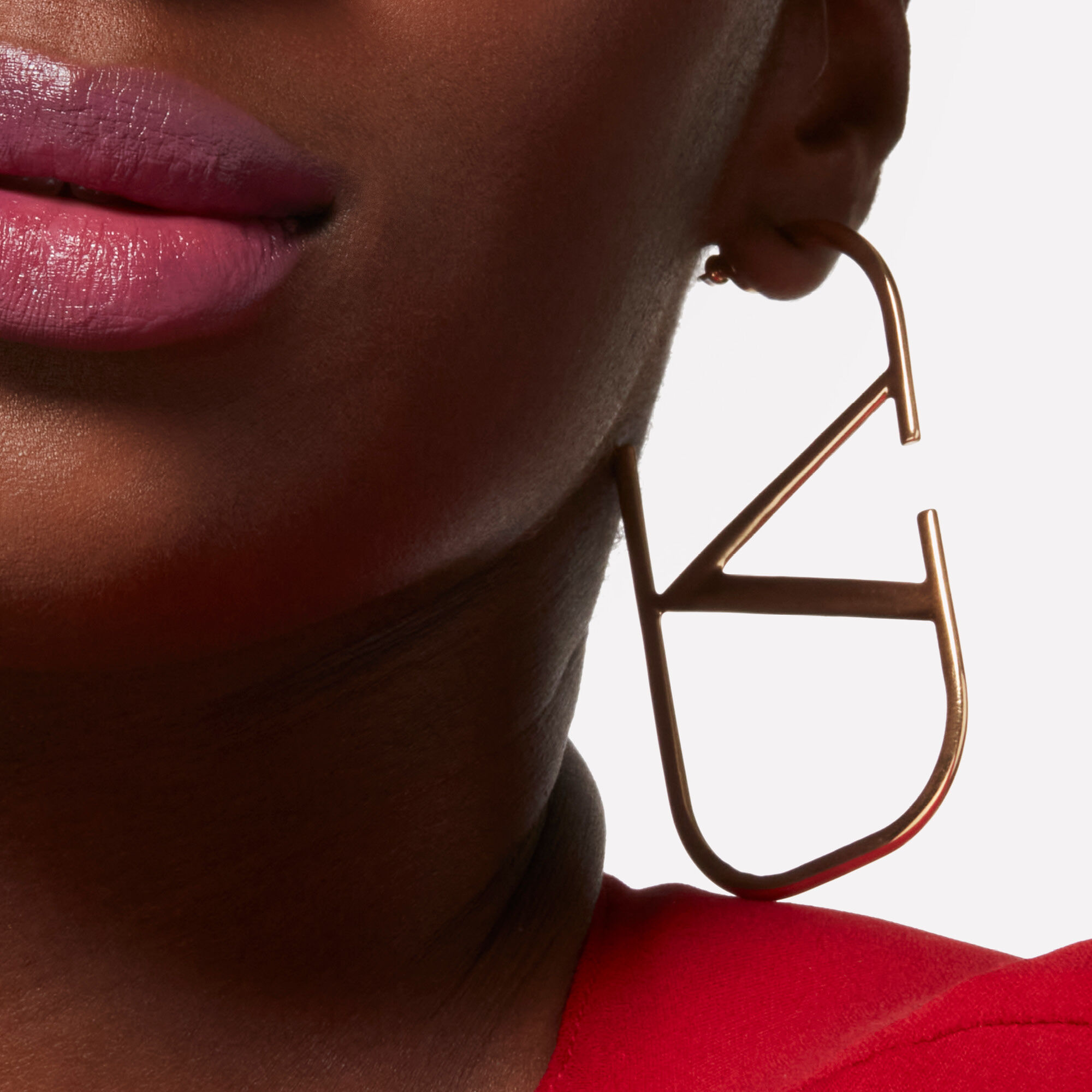 Close-up of a model's lower face wearing the Valentino Beauty logo earring
