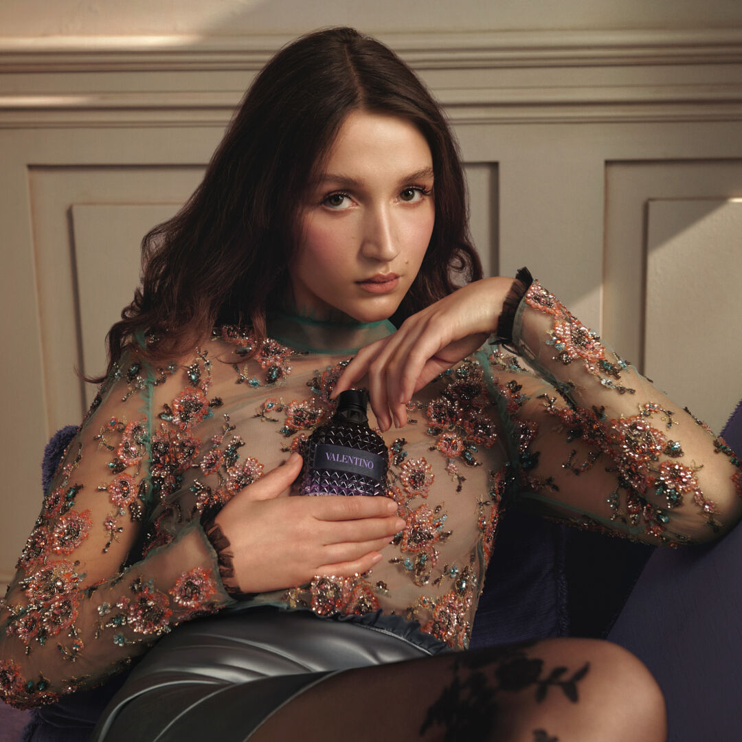 Model sitting holding a perfume bottle