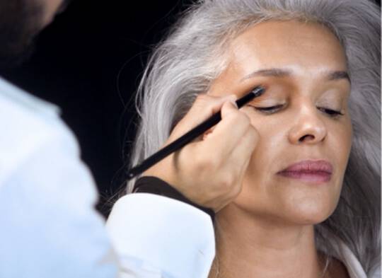 Makeup artist applying eye makeup to model with long gray hair
