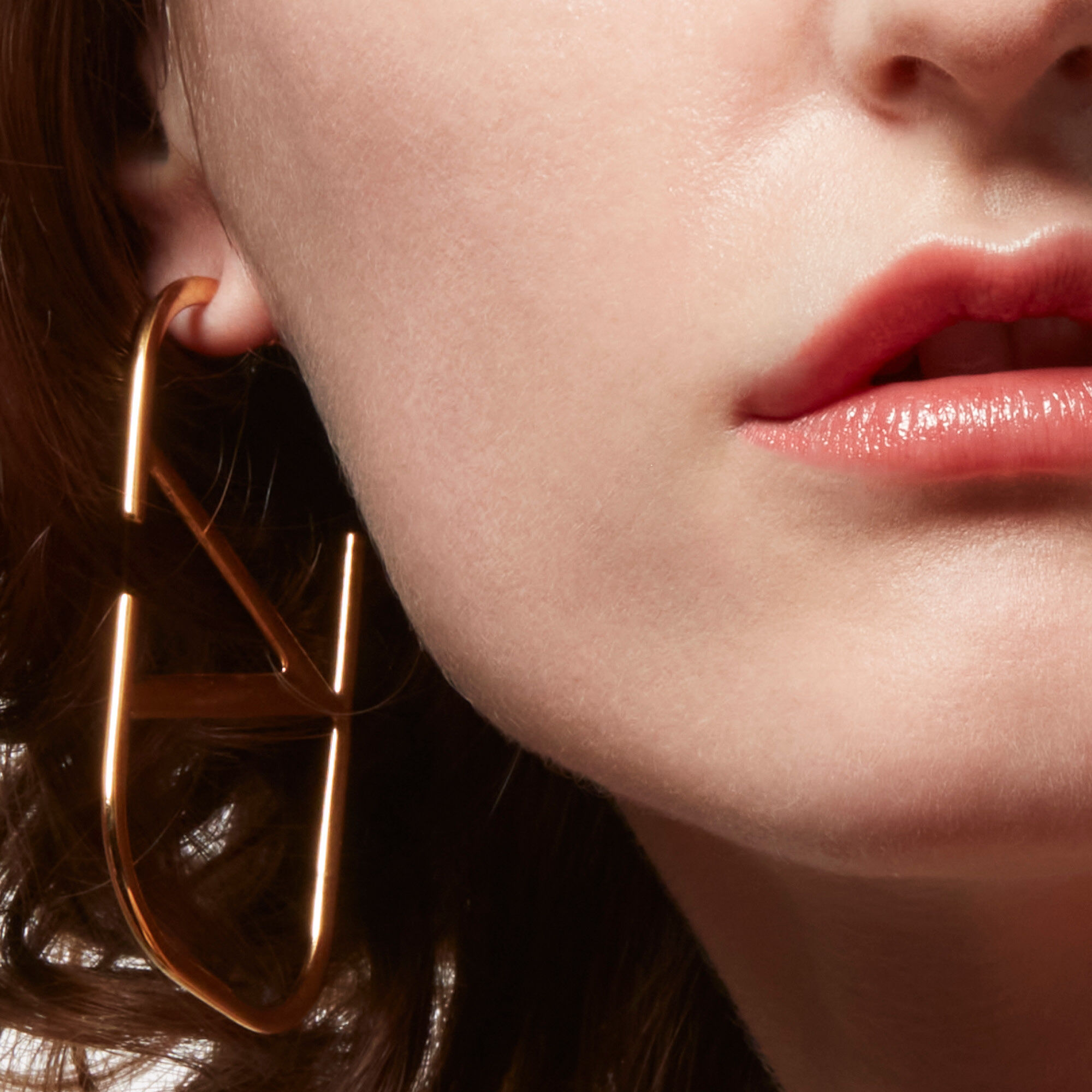 Close-up of a model's lower face wearing coral lipstick and Valentino Beauty logo earring