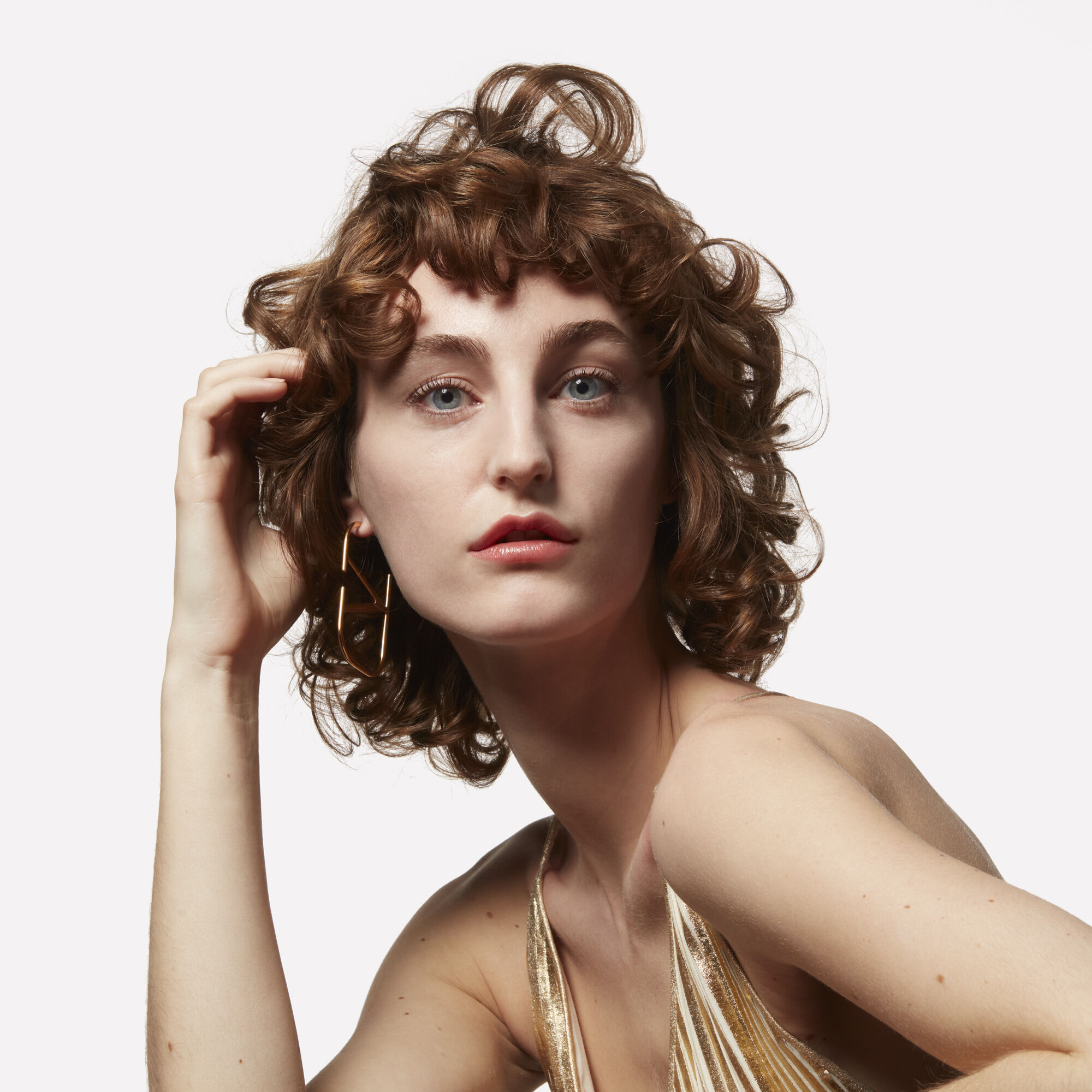A model with curly hair wearing Valentino Beauty logo earring