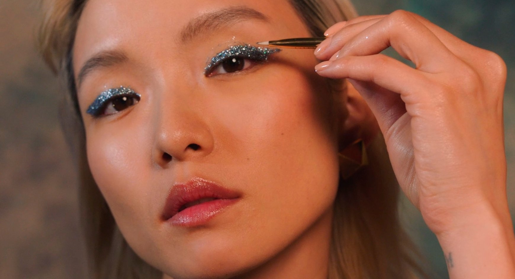 A close-up of a model applying glittery eye makeup